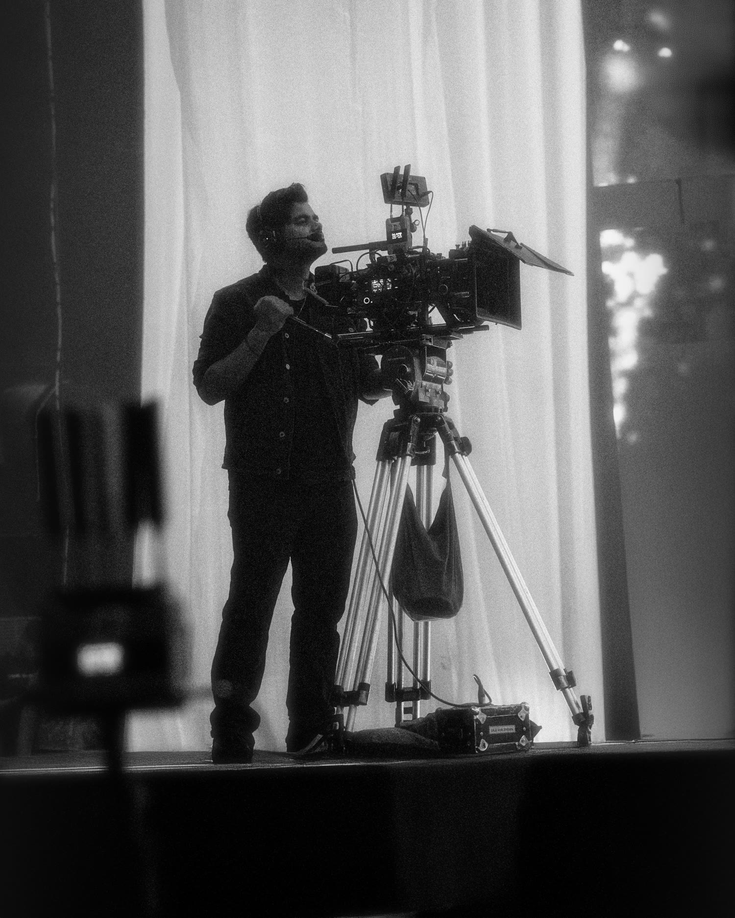 Our camera operator on a stage, headset on, behind a rigged cinema camera on a tripod.